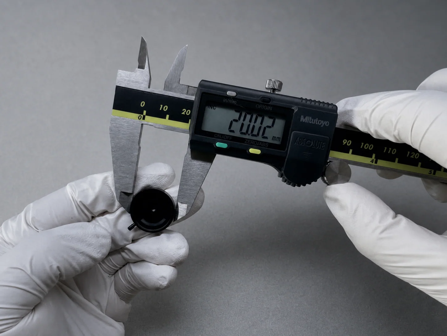 Digital caliper displaying 20.02 mm while a black iris component is measured by gloved hands