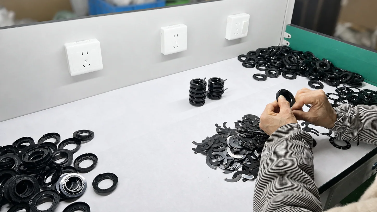 Worker assembling iris mechanisms at a bright factory workbench with components arranged around the station