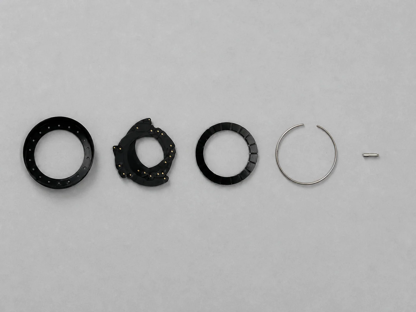 Five iris mechanism components aligned horizontally on a light gray industrial workbench