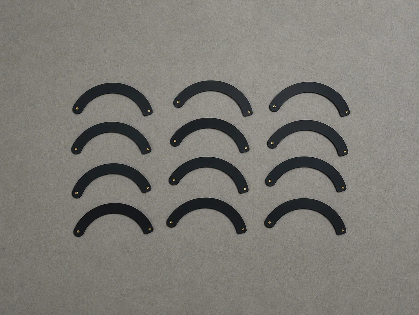 Twelve curved black iris blades arranged in a four-by-three array on a gray workbench